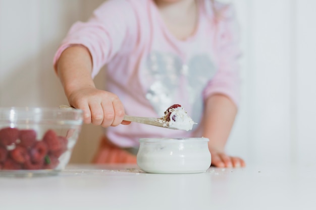 Kleines Mädchen mit Himbeere in der Creme