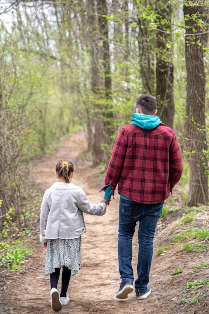 Kleines Mädchen mit Papa im Park im zeitigen Frühjahr bei kühlem Wetter, Blick von hinten.