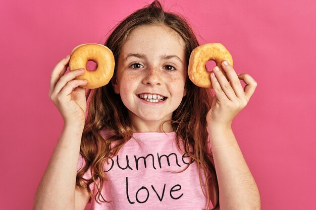 Kleines Mädchen posiert mit ein paar Donuts auf einem Rosa