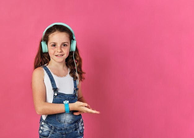 Kleines Mädchen posiert mit Kopfhörern an einer rosa Wand