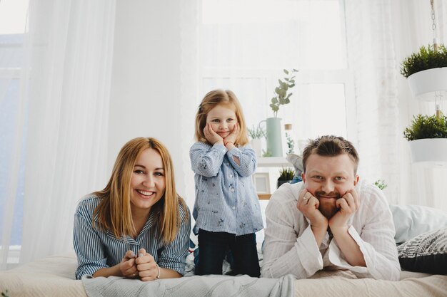 Kleines Mädchen sitzt mit ihren Eltern auf einem weißen Bett in einem hellen Raum