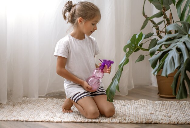 Kleines Mädchen sprüht Zimmerpflanzenblätter und kümmert sich um die Pflanze Monstera.