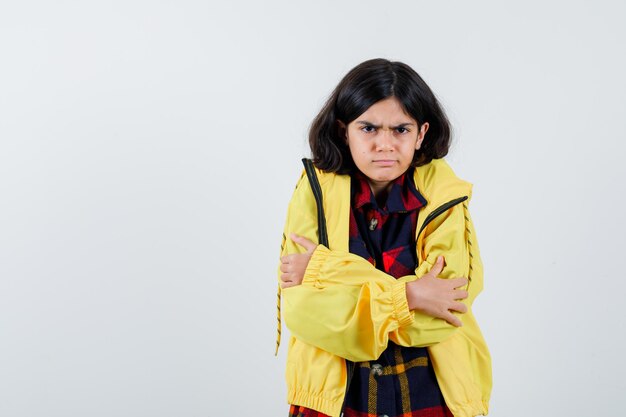 Kleines Mädchen umarmt sich in kariertem Hemd, Jacke und sieht wehmütig aus, Vorderansicht.