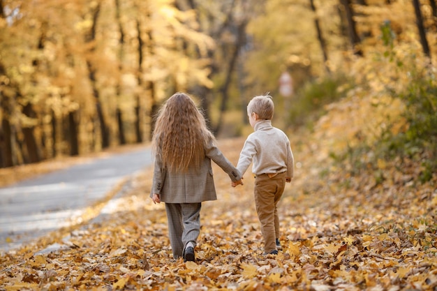 Kleines Mädchen und Junge im Herbstpark. Geschwister halten Händchen und gehen. Bruder und Schwester liegen in modischer Kleidung.