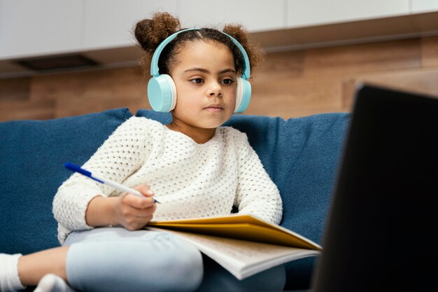 Kleines Mädchen während der Online-Schule mit Laptop und Kopfhörern
