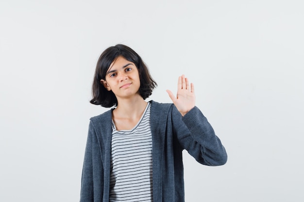 Kleines Mädchen winkt Hand, um sich in T-Shirt, Jacke zu verabschieden und selbstbewusst auszusehen