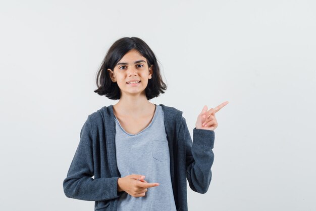 Kleines Mädchen zeigt auf die obere rechte Ecke in T-Shirt, Jacke und sieht selbstbewusst aus