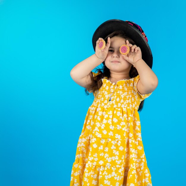 Kleines schönes lächelndes Mädchen mit einem lustigen Gesicht in einem gestreiften gelben Kleid, das auf einem blauen Hintergrund im Studio posiert