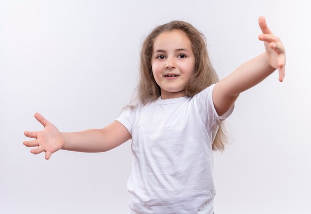 kleines Schulmädchen, das weißes T-Shirt trägt, das Größe auf isolierter weißer Wand zeigt