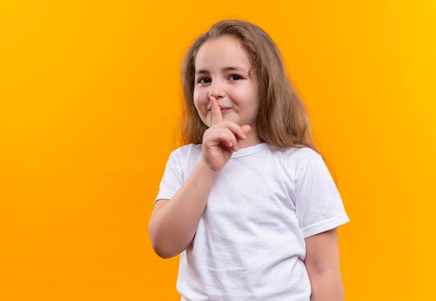 kleines Schulmädchen, das weißes T-Shirt trägt, das Stille Geste auf isolierter orange Wand zeigt