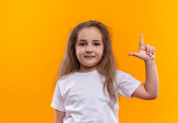kleines Schulmädchen, das weißes T-Shirt trägt, legte ihren Finger auf isolierte orange Wand