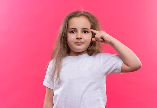 kleines Schulmädchen, das weißes T-Shirt trägt, legte ihren Finger auf Stirn auf isolierte rosa Wand