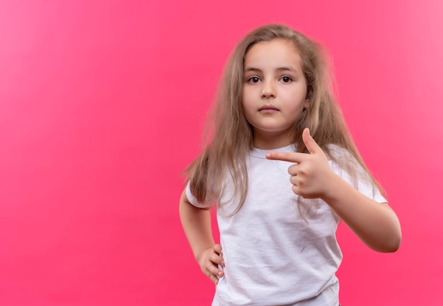 kleines Schulmädchen, das weißes T-Shirt trägt, zeigt zur Seite auf isolierter rosa Wand