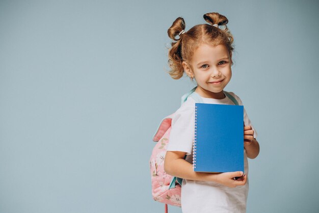 Kleines Schulmädchen mit Notebook und Rucksack im Hintergrund isoliert
