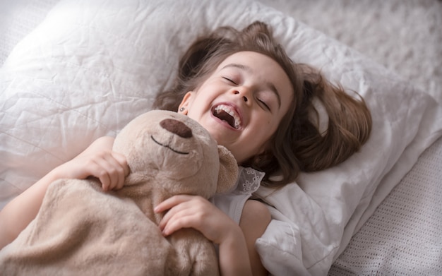 Kleines süßes Mädchen im Bett mit Spielzeug