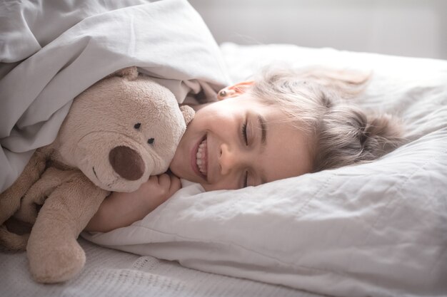 Kleines süßes Mädchen im Bett mit Spielzeug