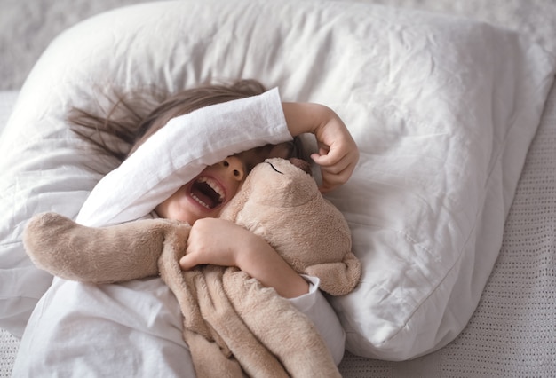 Kleines süßes Mädchen im Bett mit Spielzeug