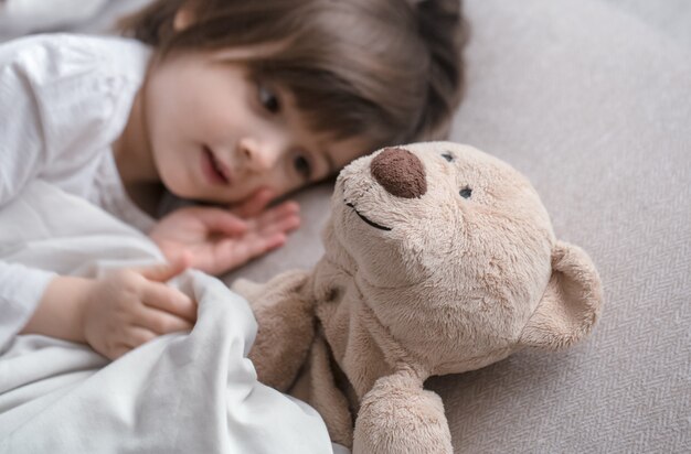Kleines süßes Mädchen im Bett mit Spielzeug