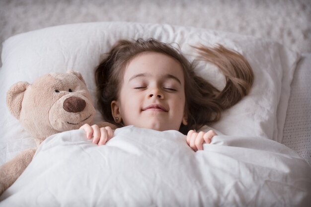 Kleines süßes Mädchen im Bett mit Spielzeug