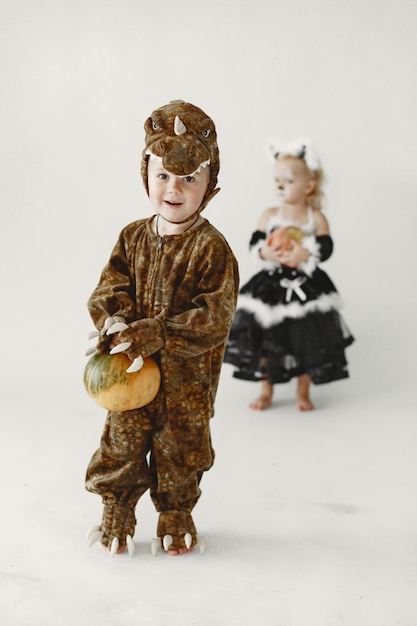 Kleinkind des kleinen Jungen gekleidet im braunen Kostüm eines Dinosauriers, der einen Kürbis hält. Junge hat eine Kapuze mit Dino-Gesicht