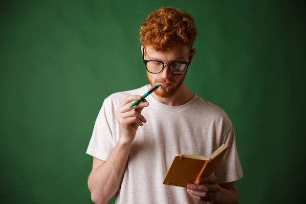 Kluger bärtiger Student mit Lesekopf in Brille, der die Notizen mit Stift in seinem Mund liest