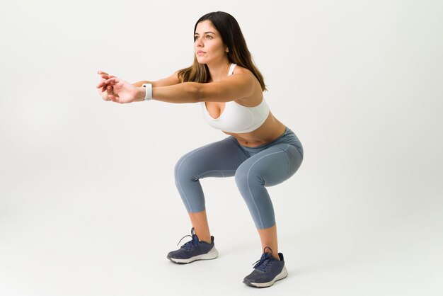 Kniebeugen sind die beste Übung für deine Beine. Fitness schlanke Frau in Activewear beim Squat-Training vor weißem Hintergrund