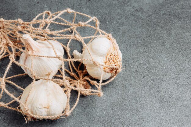 Knoblauch mit hoher Winkelansicht im Netzbeutel auf dunklem strukturiertem Hintergrund. horizontal