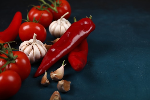 Knoblauchhandschuhe, Tomaten und Pfeffer des roten Paprikas auf einem blauen Hintergrund.