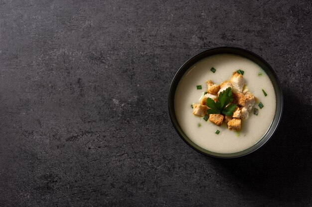 Knoblauchsuppe mit Croutons in Schüssel auf schwarzem Schieferhintergrund