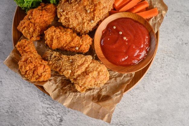 Knusperiges gebratenes Huhn auf einer hölzernen Platte mit Tomatensauce und Karotte