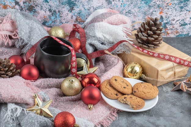 Knusprige Ingwerkekse in einer weißen Untertasse mit einer Tasse Getränk und Weihnachtsschmuck herum