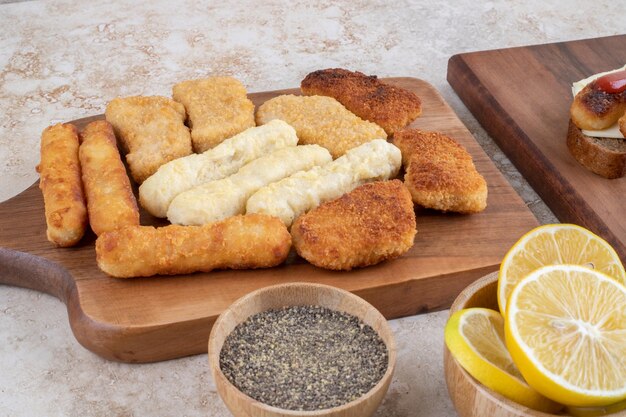 Knusprige Nuggets, Käsesticks und Grillwürstchen auf einer Holzplatte.