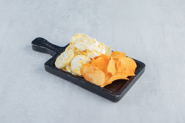 Knusprige Vollkornreiskuchen und -chips auf schwarzem Schneidebrett.