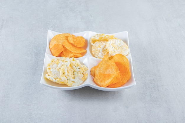 Knusprige Vollkornreiskuchen und würzige Chips in weißen Schalen.