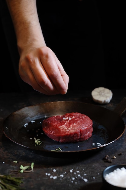 Koch, der frisches Fleisch an Bord kocht Dunkler Hintergrund Kochkonzept