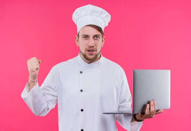 Koch, der Kamera betrachtet, gewinnt Ausdruck auf Gesicht mit Notizbuch auf Hand, das über rosa Wand steht