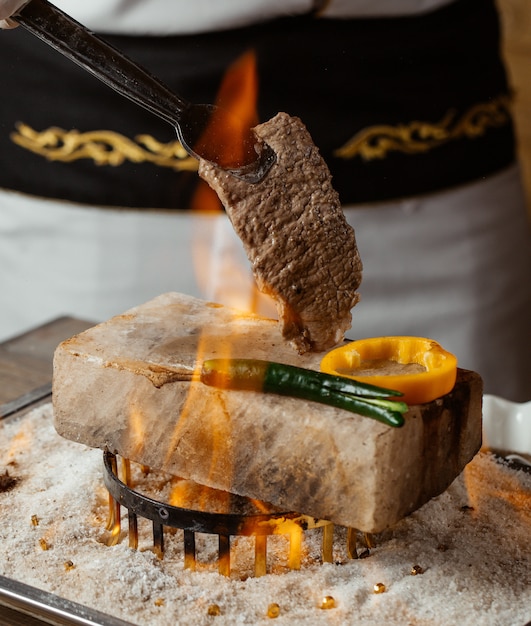 Koch hält Rindersteak auf Stein mit gegrillten Paprika in Brand