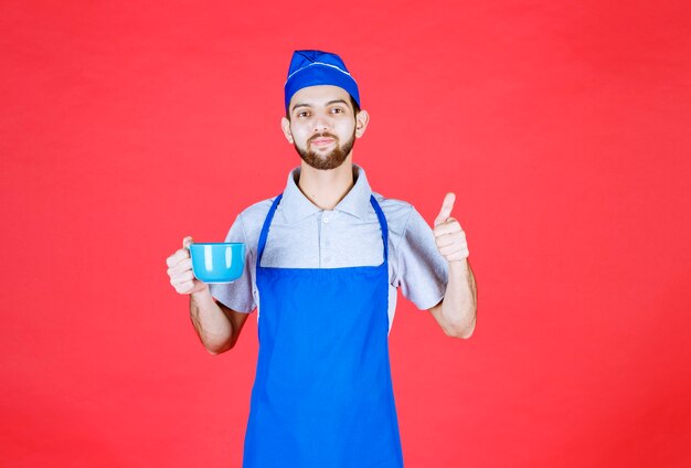 Koch in blauer Schürze, die eine blaue Keramiktasse hält und den Geschmack des Produkts genießt.