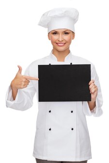 Koch-, werbe- und lebensmittelkonzept - lächelnde köchin, köchin oder bäckerin, die mit dem finger auf leeres schwarzes papier zeigt