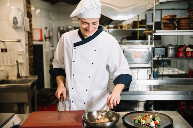 Kochen Sie bei Tisch stehen mit Fleisch und Salat