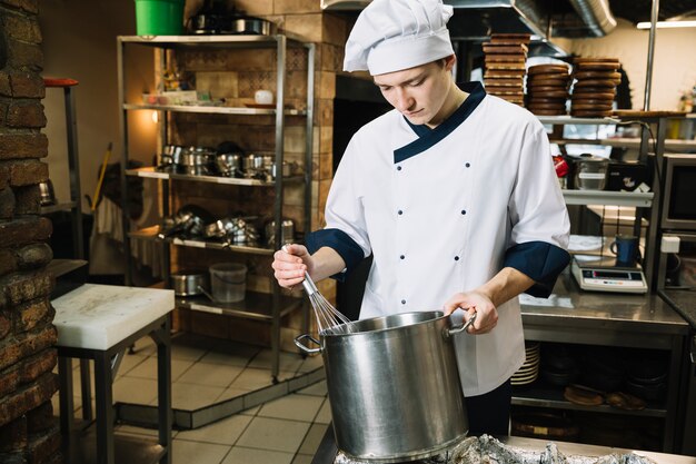 Kochen Sie, indem Sie etwas im Topf mit Schneebesen schlagen