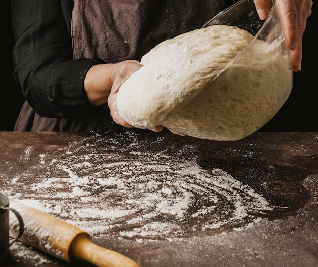 Köchin der Frau, die Pizzateig auf einen mit Mehl bedeckten Tisch gießt