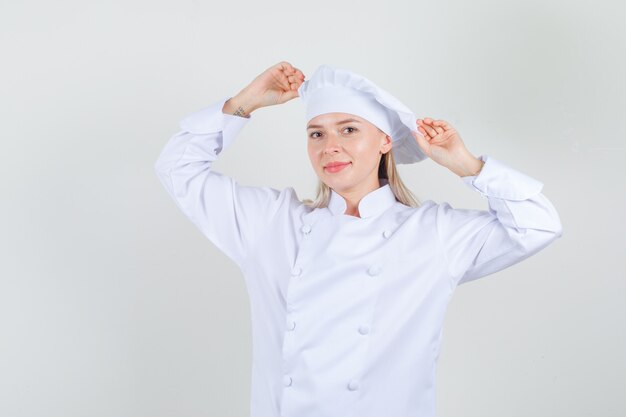 Köchin, die ihren Hut in der weißen Uniform hält und fröhlich aussieht