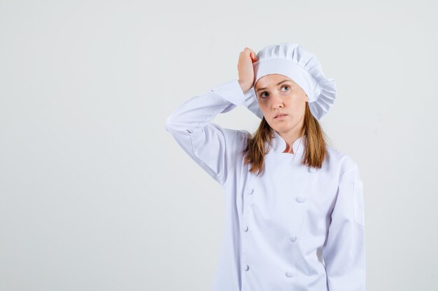 Köchin, die mit Hand auf Kopf in der weißen Uniform nach oben schaut und verwirrt schaut