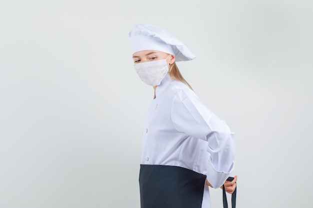 Kostenloses Foto köchin, die schürze um taille in weißer uniform, medizinische maske bindet.