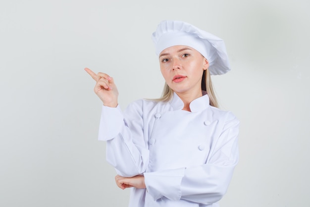 Kostenloses Foto köchin in weißer uniform, die finger zur seite zeigt und selbstbewusst aussieht