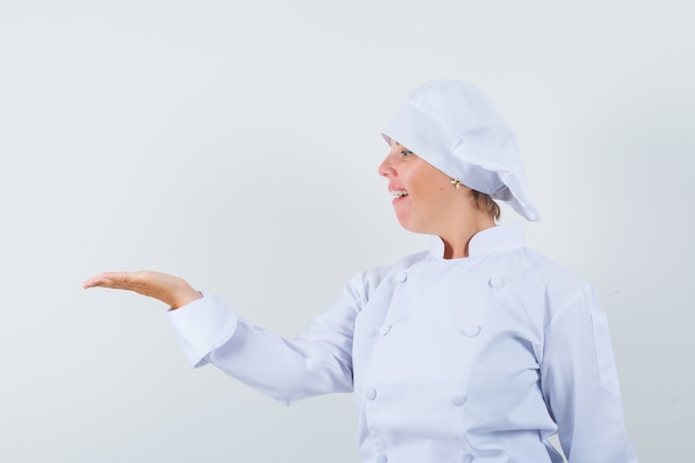 Köchin in weißer Uniform, die ihre Handfläche betrachtet und stolz aussieht