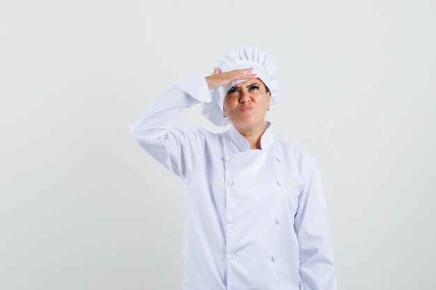 Köchin in weißer Uniform, die mit Hand über Augen nach oben schaut