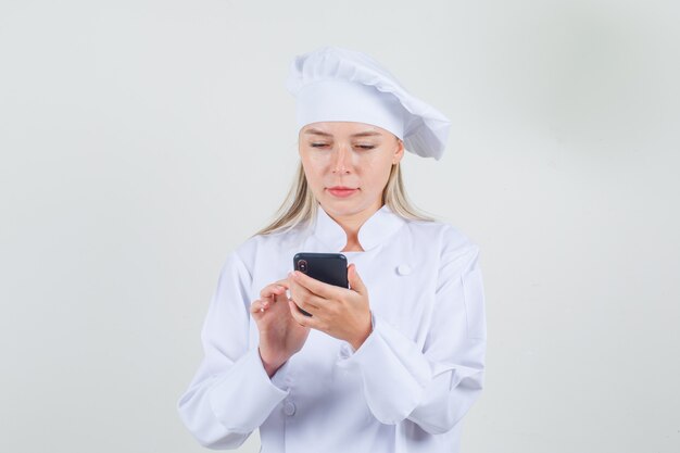 Köchin in weißer Uniform mit Smartphone und Blick beschäftigt