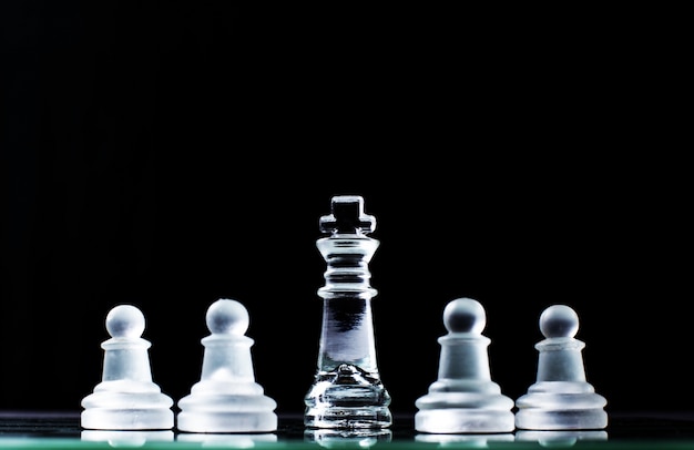 König und mehrere Schachfiguren auf Schachbrett in dunklem Hintergrund. Hierarchie-Konzept.